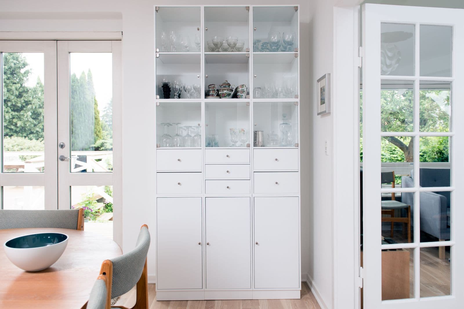 A tall white glass-fronted cabinet holding rows of glassware in a bright room