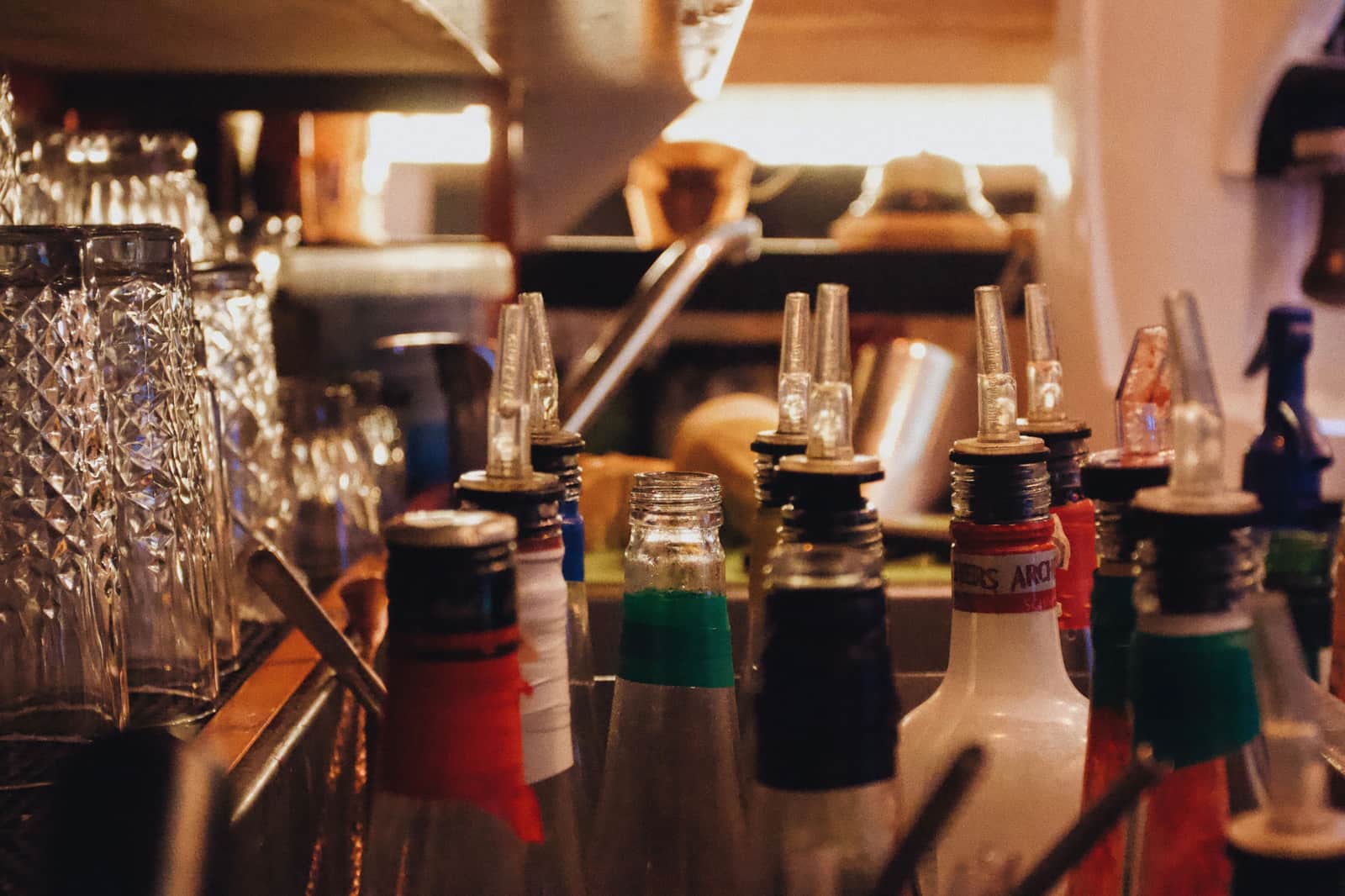 Spirit bottles fitted with pour spouts lined up along a bar