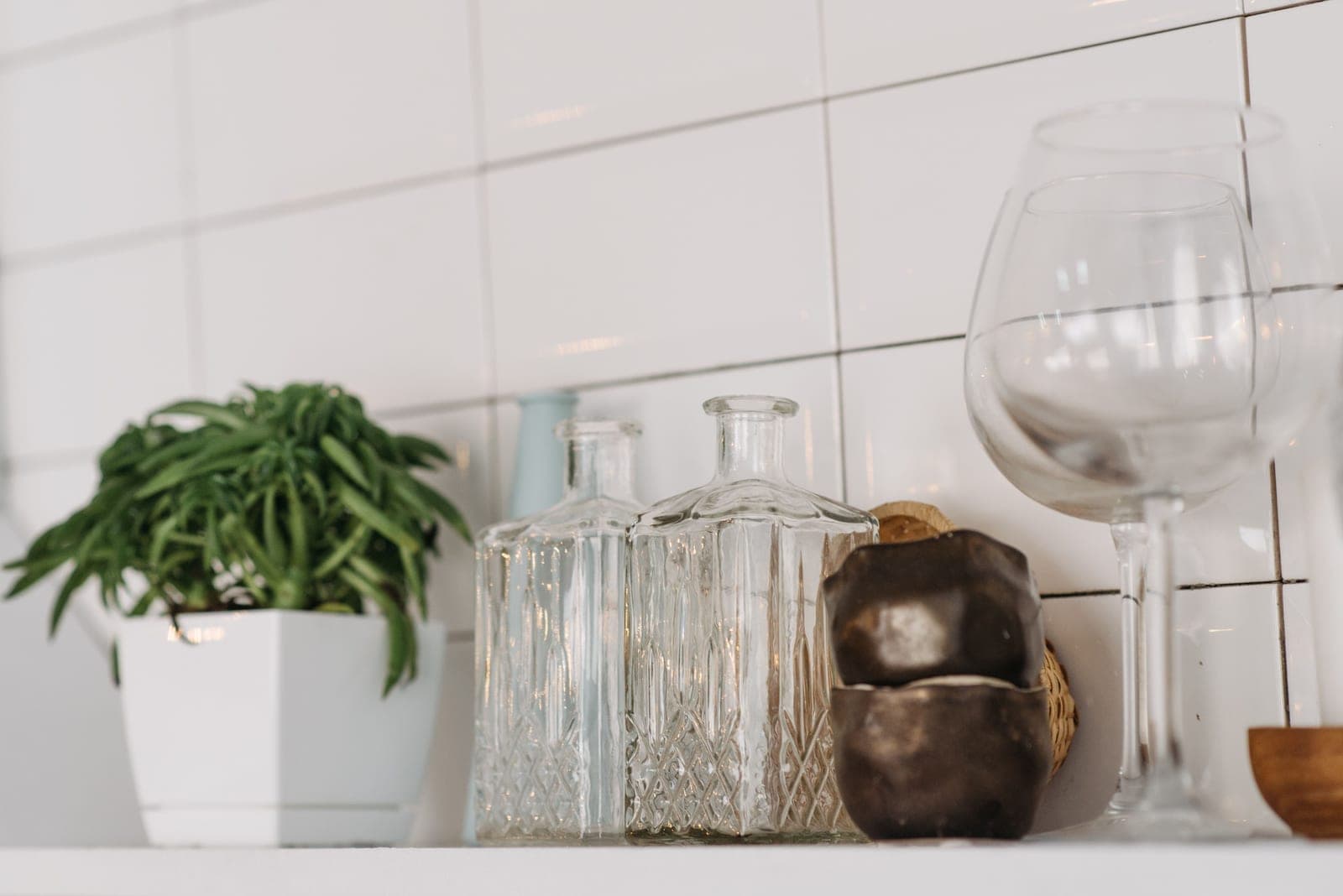 Glassware and bottles arranged on a bright kitchen shelf beside a plant