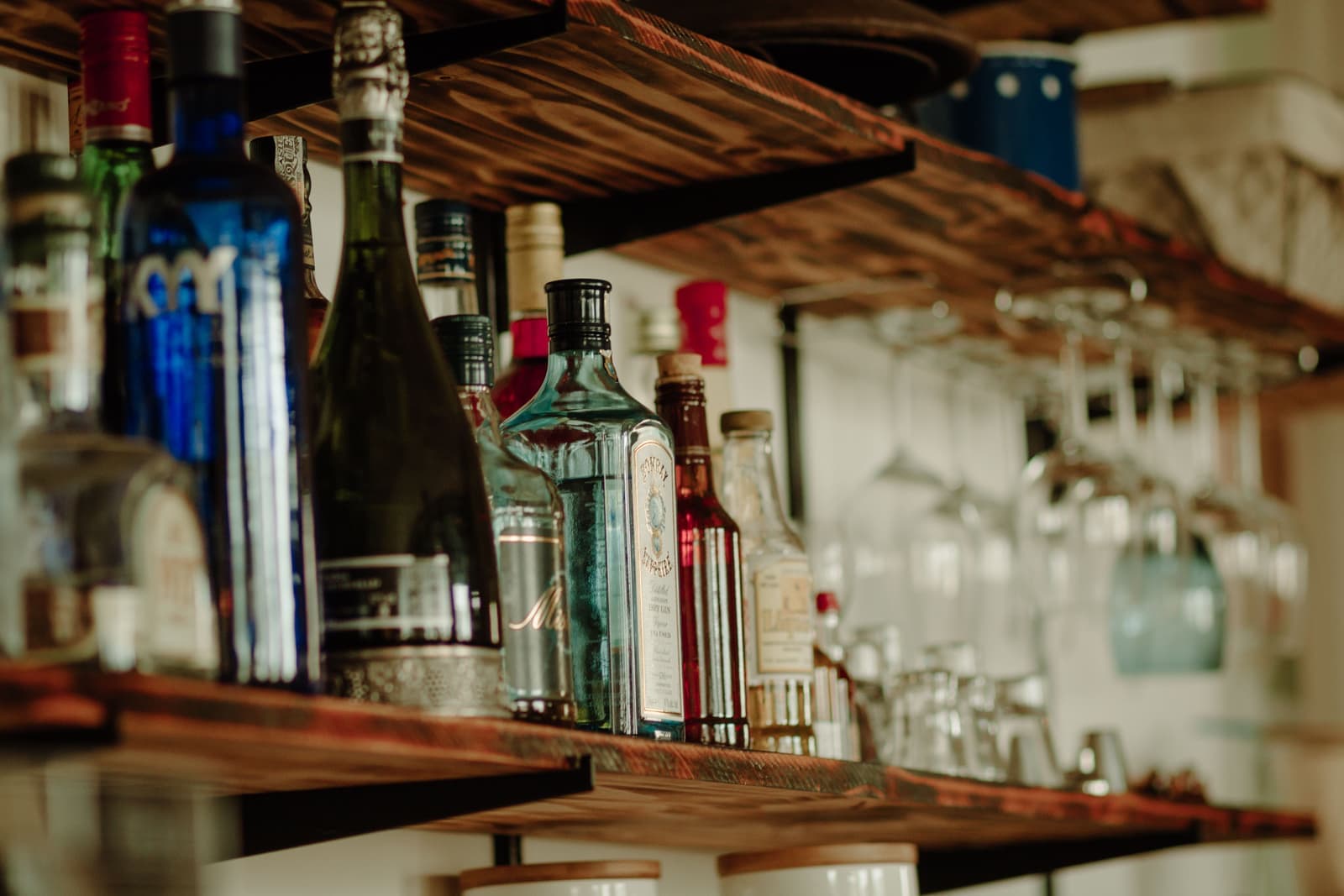Bottles and hanging glassware on a narrow home bar shelf