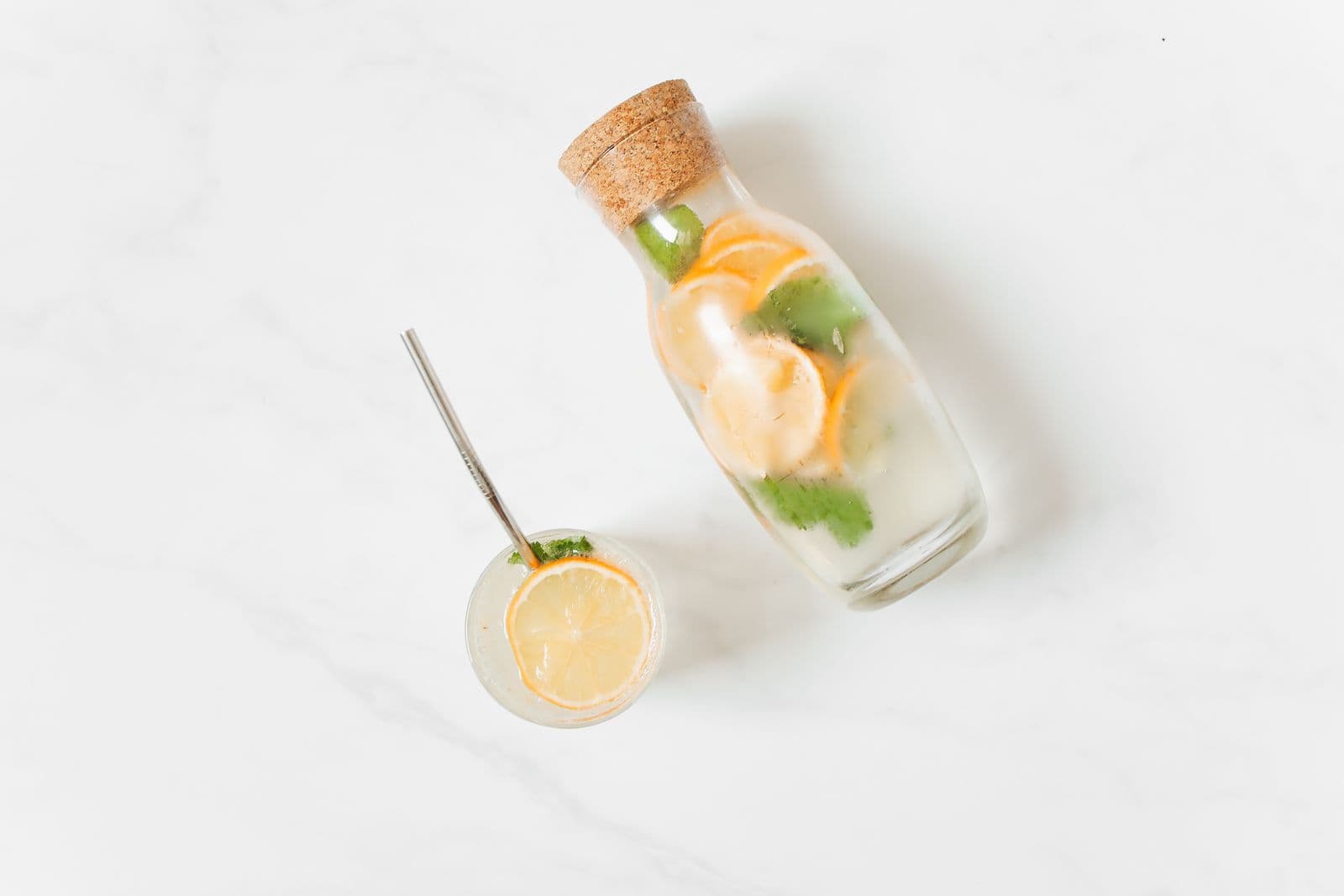 Citrus and mint in a glass and a jar, shot from above on a pale surface