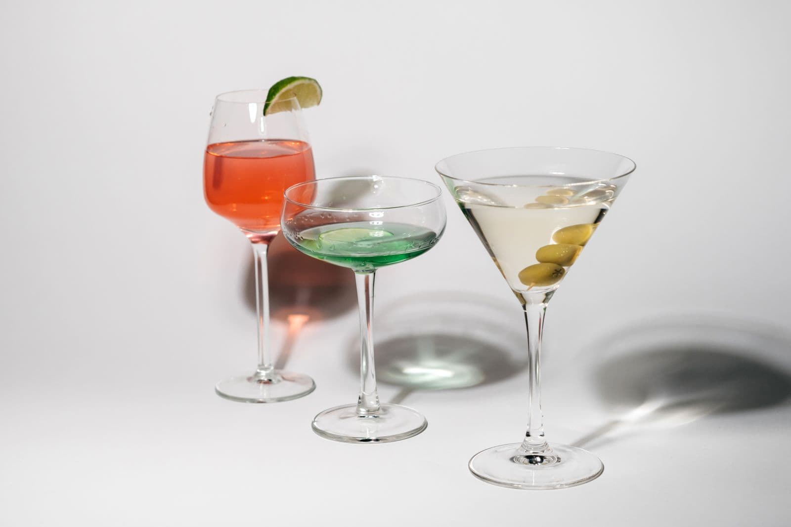 Three cocktails with lime and olive garnishes against a pale background
