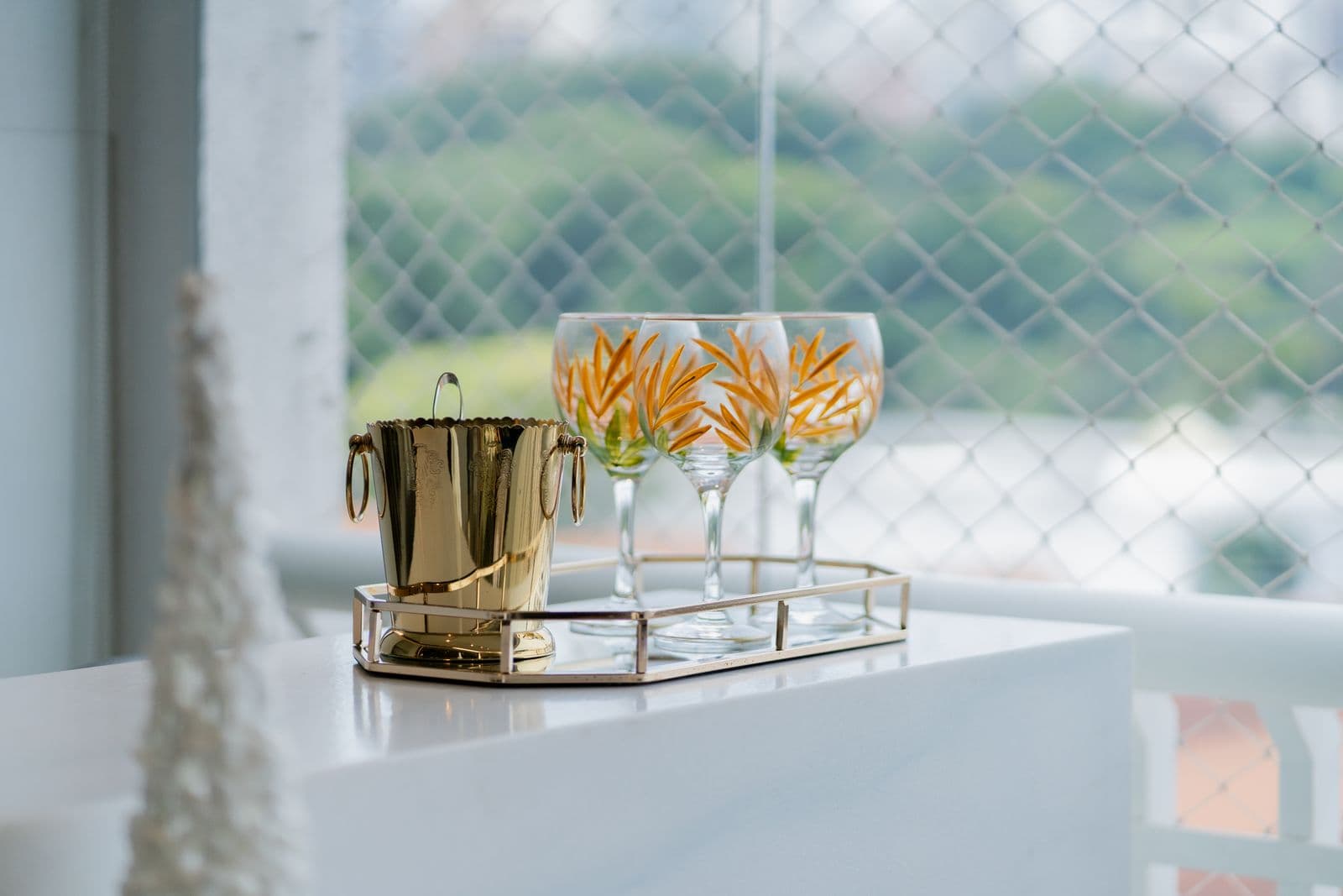 A gold ice bucket and a gold-framed tray of stemmed glasses on a bright white counter