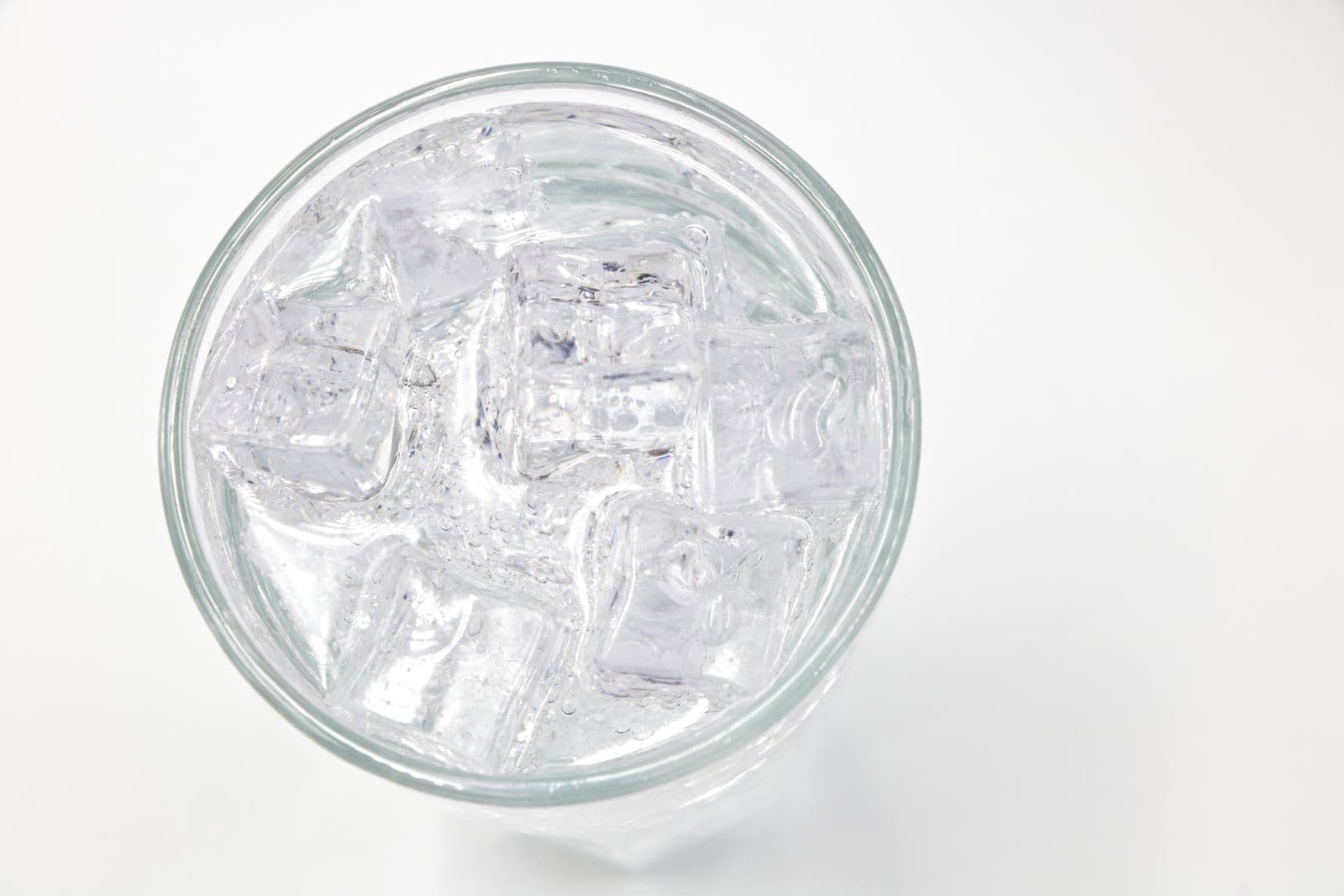 A glass filled with ice cubes and water, shot from above on a pale surface