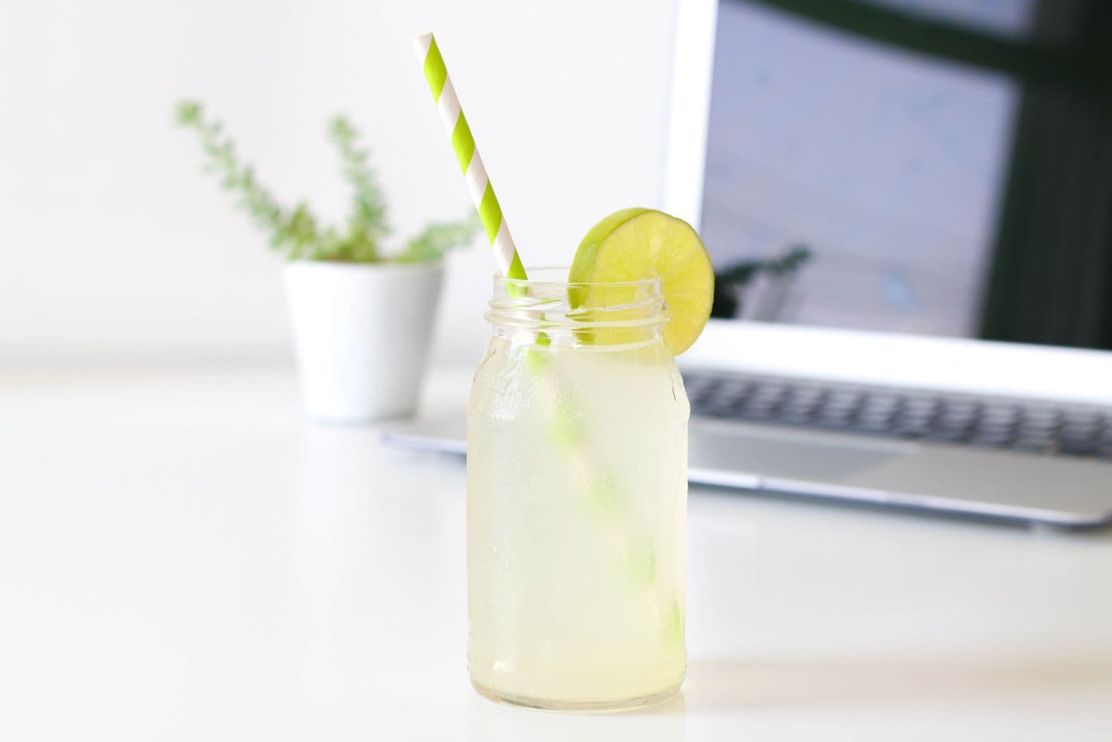 A citrus drink with a lime wheel served in a glass jar on a bright desk