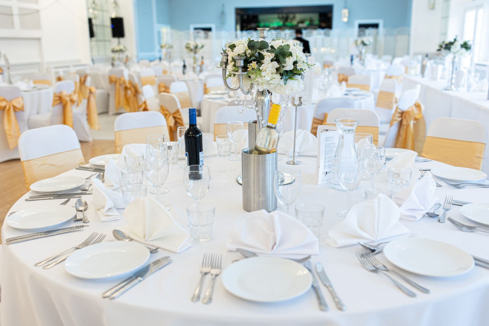 A wedding reception table set with white linen, glassware and a floral centerpiece