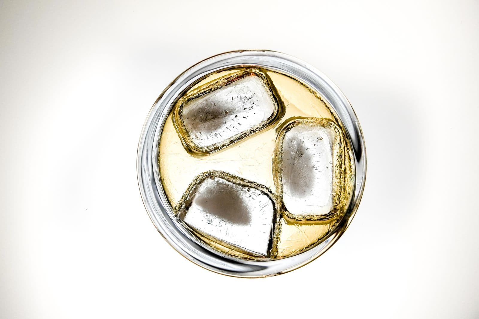 A chilled drink with ice cubes in a clear glass, shot from above against white