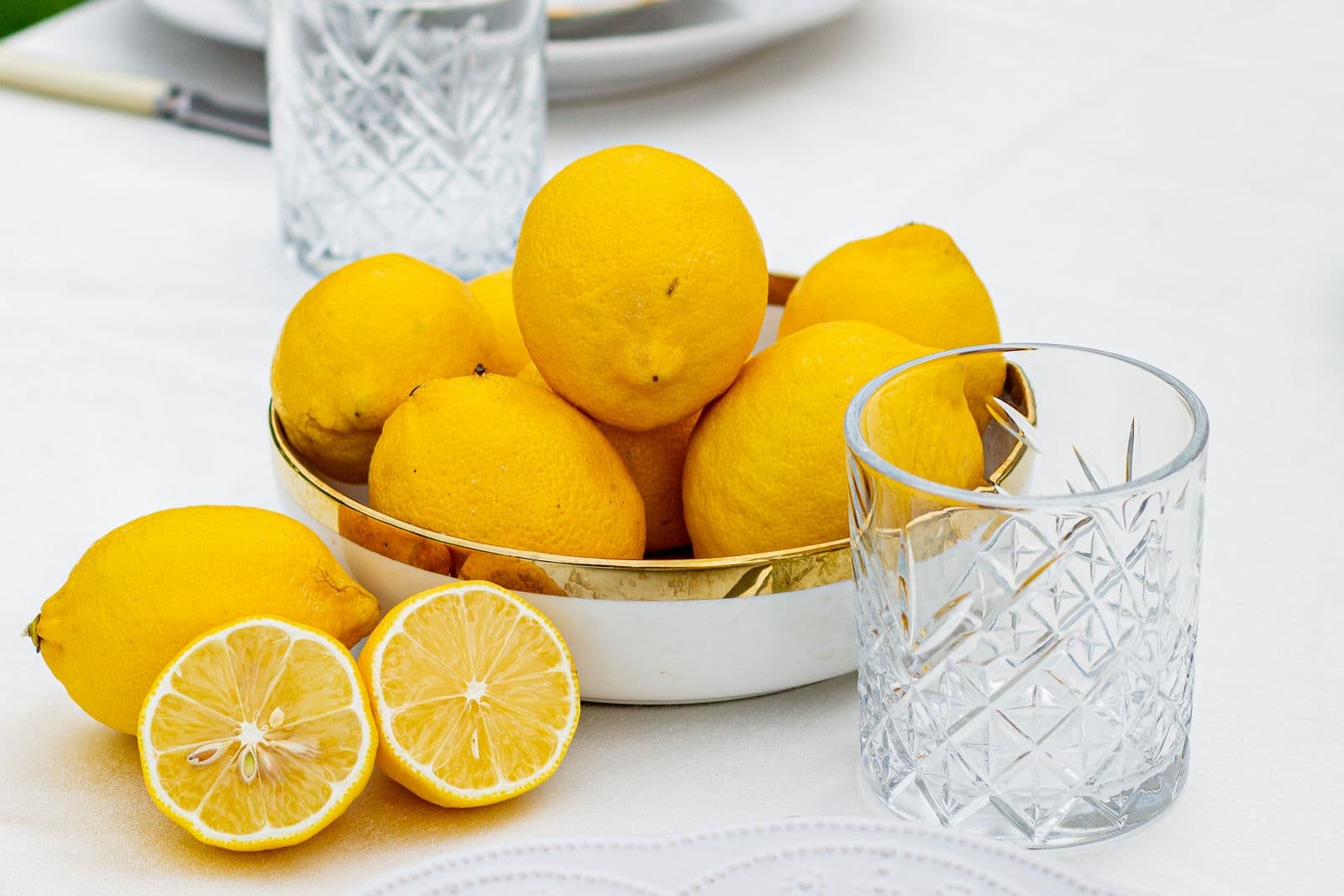A bowl of lemons beside cut-crystal glasses on a white table