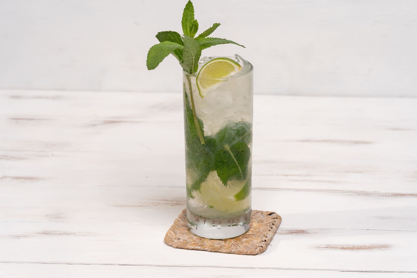 A tall mojito with mint and lime on a white surface