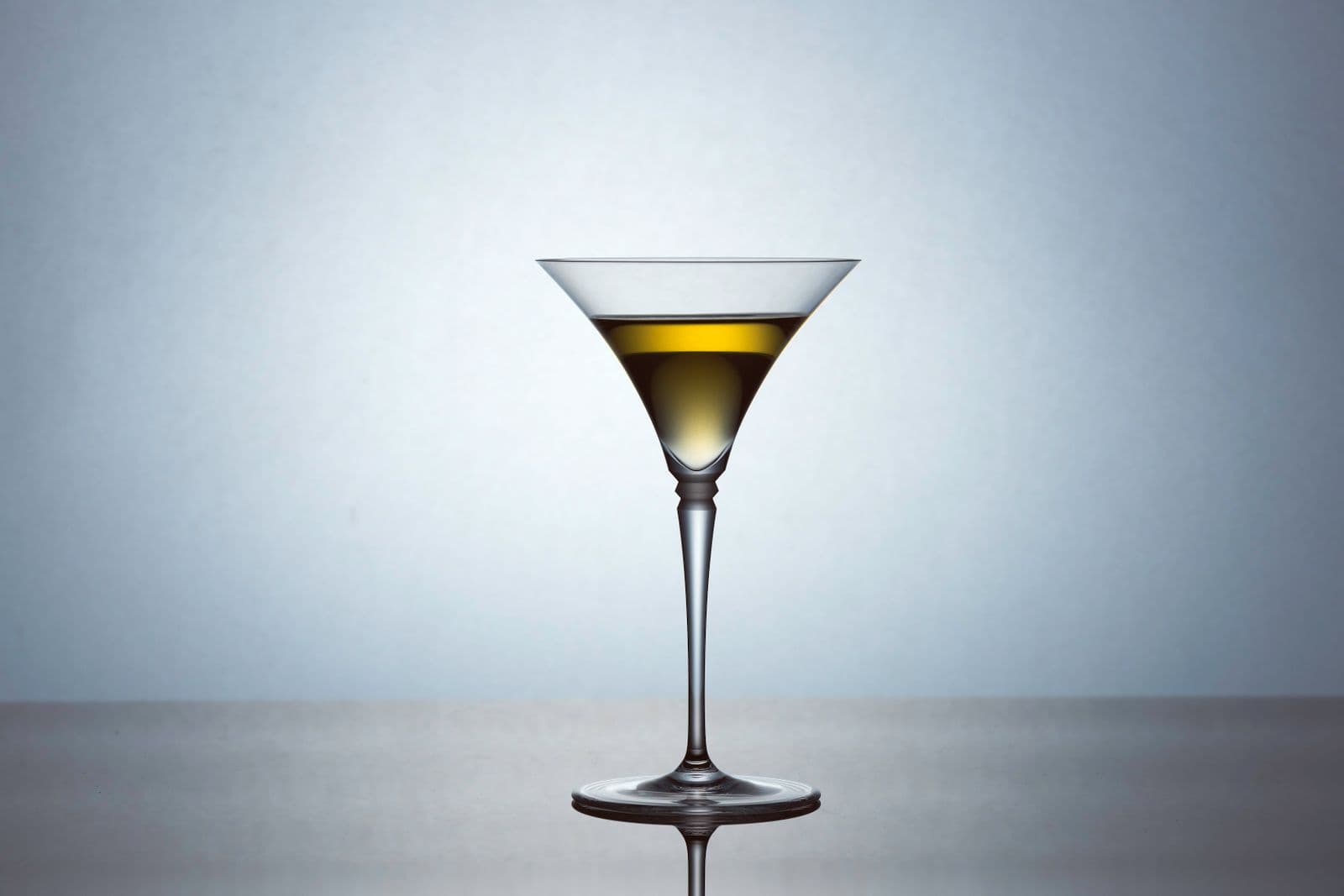 A martini glass with an olive-tinted drink against a pale background