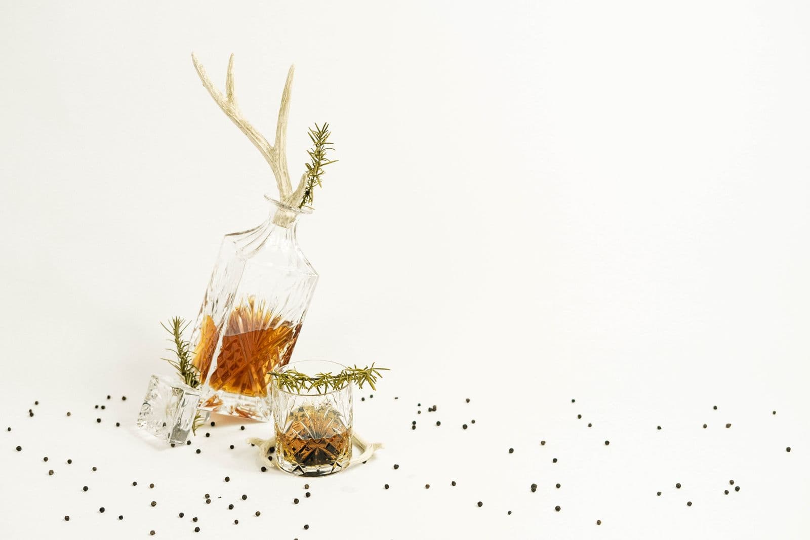 A carafe and a glass of amber spirit with rosemary sprigs on a bright table