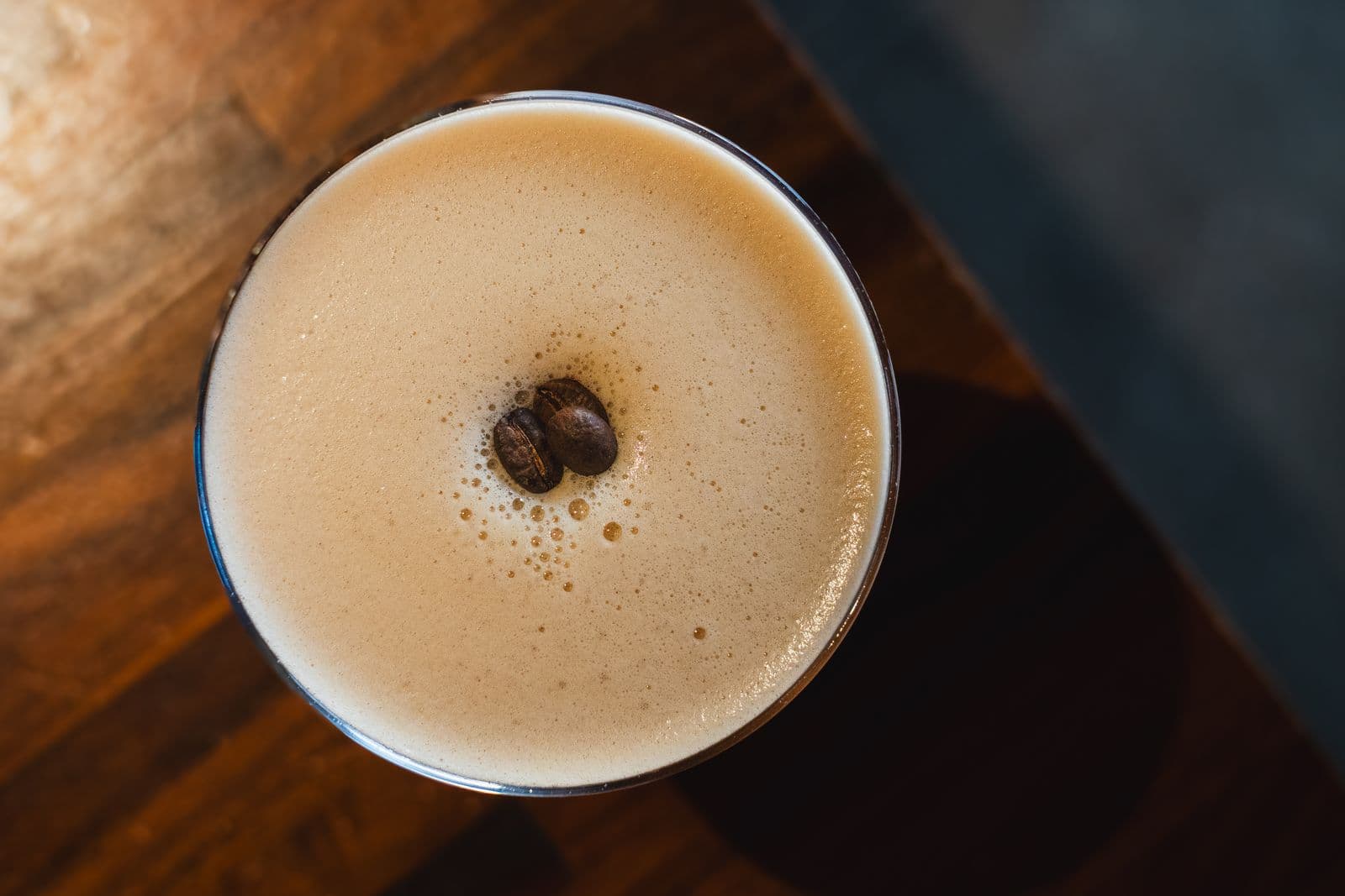 A frothy espresso martini garnished with coffee beans, shot from above