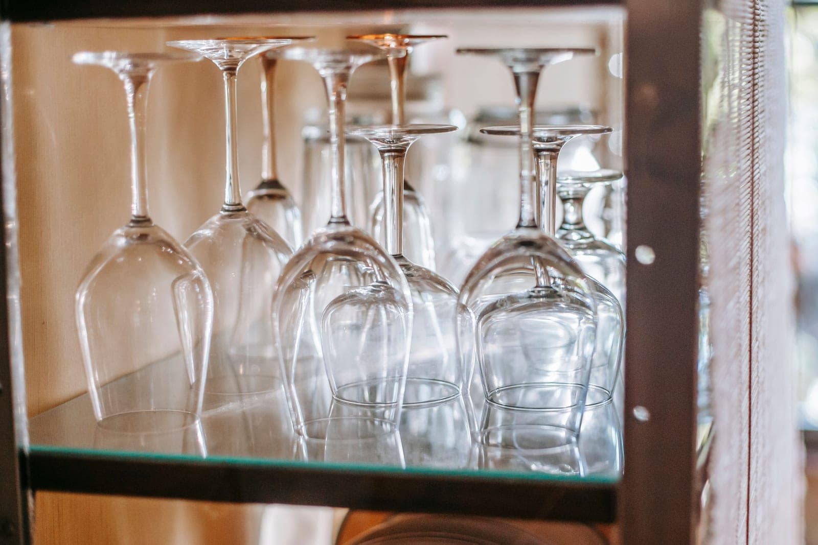 Stemmed and stemless glasses standing upside down on a lit glass shelf