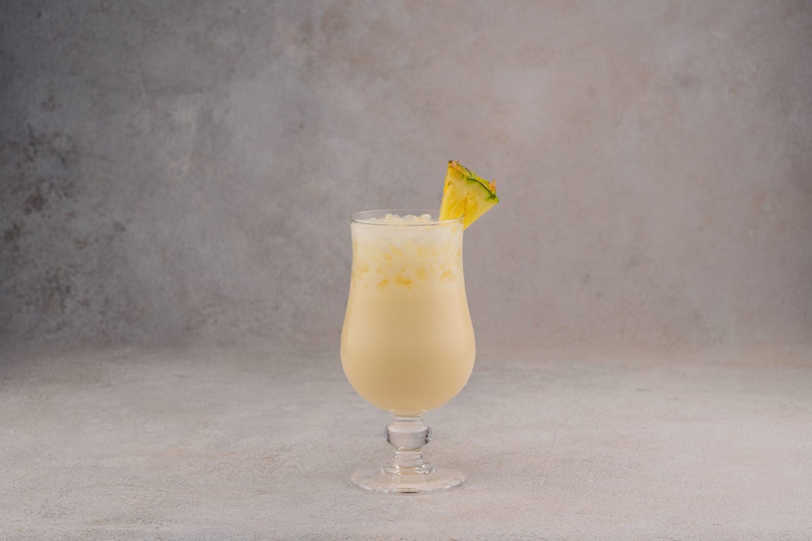 A creamy pina colada in a tall footed hurricane glass with a pineapple wedge