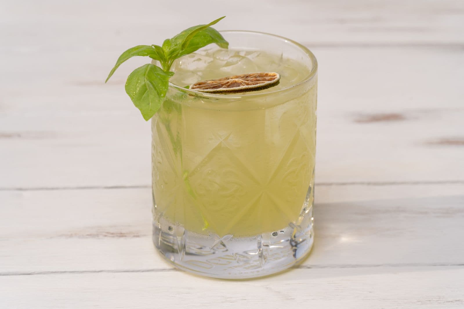 A mint-garnished cocktail in a faceted rocks glass on a pale surface