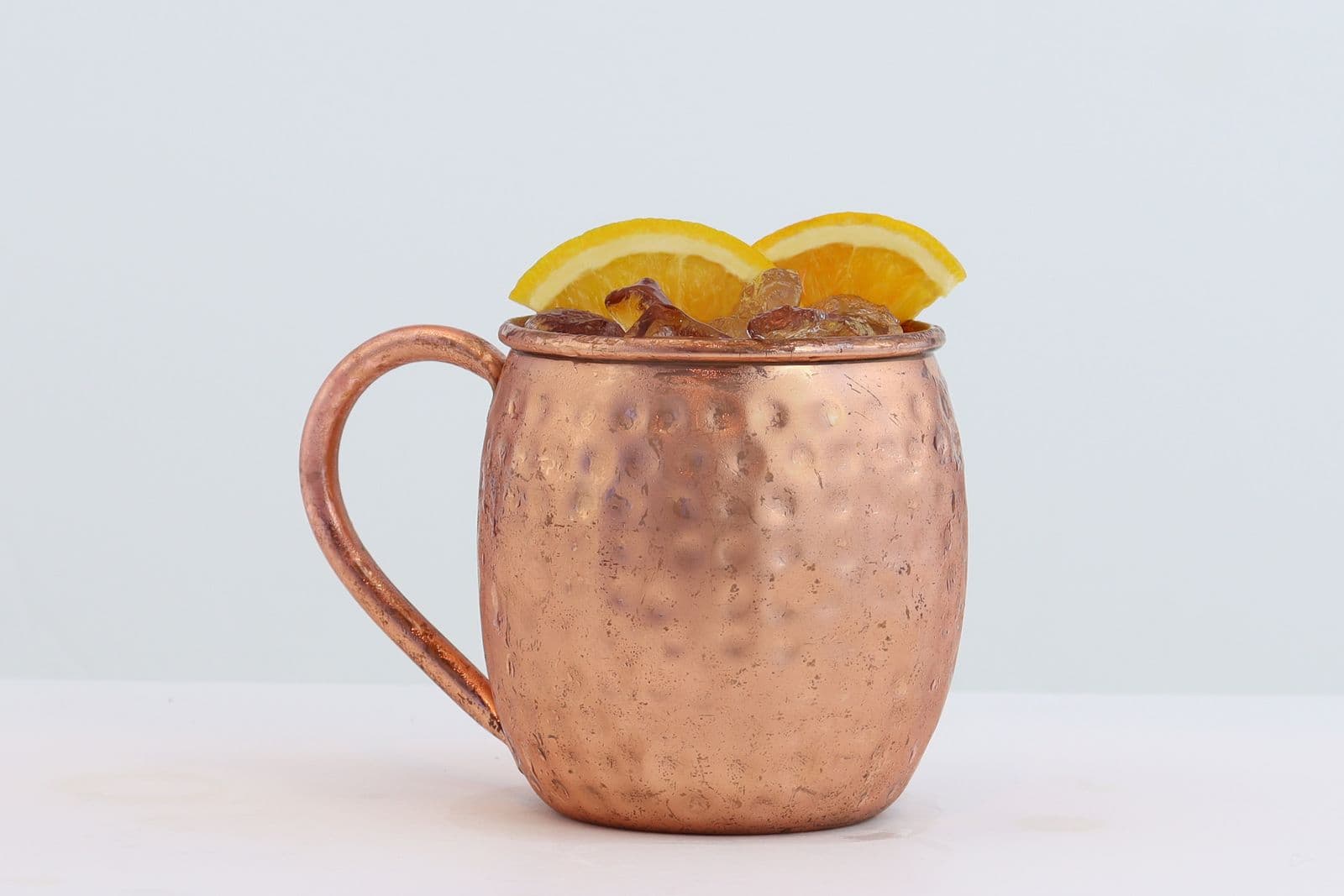 A hammered copper mule mug with citrus slices on a white background