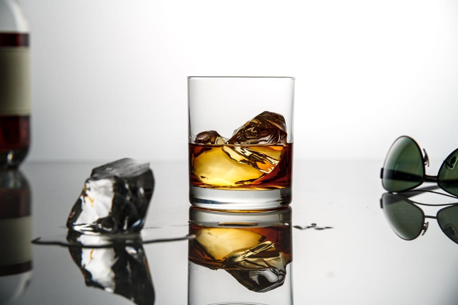 A whiskey glass with ice on a bright reflective surface