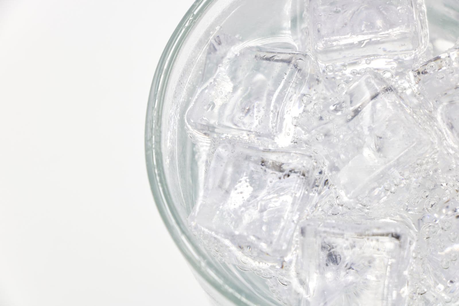 A glass of sparkling water filled with ice on a white background