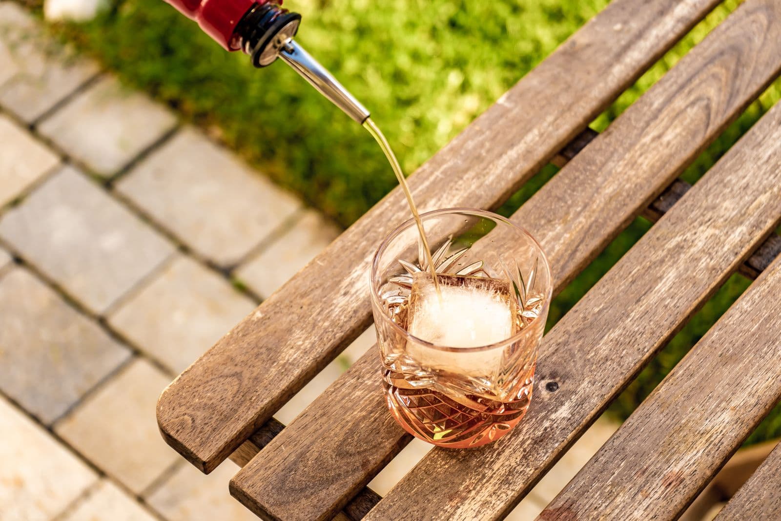 A drink being poured over a large ice cube in a glass