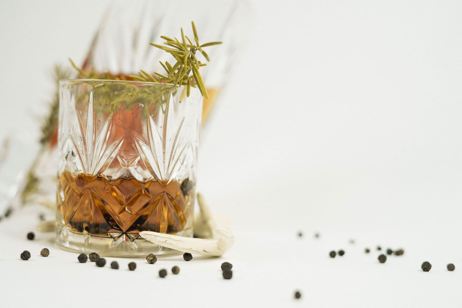 A glass of whiskey with a rosemary sprig on a pale table